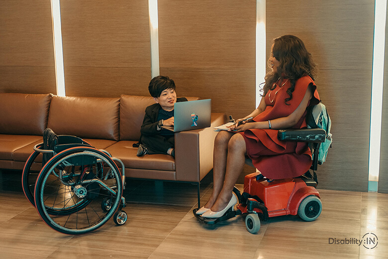 Women with a disability in a discussion, one with a laptop and the other taking notes.